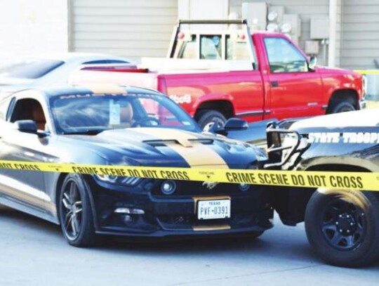 The Ford Mustang Brandon Cruz reportedly was sitting in when he was fatally shot on Monday is pressed against a Texas Highway Patrol vehicle in the back of the Carrington Place Apartments complex on Mondat afternoon. Star photo by Keith E. Domke