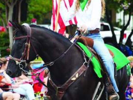 A Kendall County 4-H member rides a horse while she carries the American flag during Saturday’s fair parade along Boerne’s Main Street. Star photo by Keith E. Domke