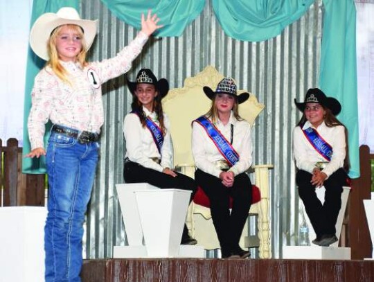 Emma Schulze, the new Kendall County Fair Association’s Little Miss, waves to the audience during Thursday’s pageant. Pictured behind her are outgoing fair queen court members Junior Miss Makenna Jureczki, Queen Sushanna Cobb and Little Miss Kaci Lemm. Star photo by Keith E. Domke