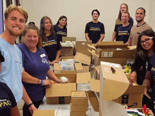 Volunteers join Hunter Beaton, second from left, spend time stuffing backpacks with essential items.