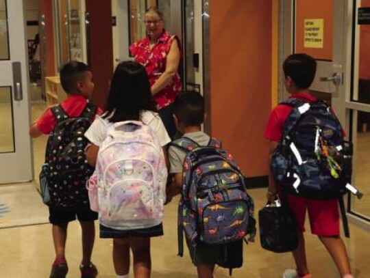 Lauri Saur, Principal Jennifer Hammond’s secretary, holds the door for a group of students entering Herff Elementary on the first day of school Thursday.