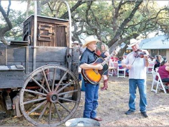 Providing classic western music for attendees to Wednesday’s Frost Bank chuck wagon breakfast were guitarist Weyman Mc-Bride, left, and fiddler Ron Knuth. Meanwhile, Rick Fairchild, left, of Double Wells Wagon and Catering, of Hunt Texas, stirs a skille